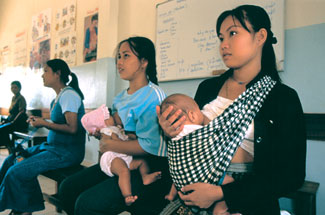 Two mothers sit on a bench together; each is breastfeeding her baby.